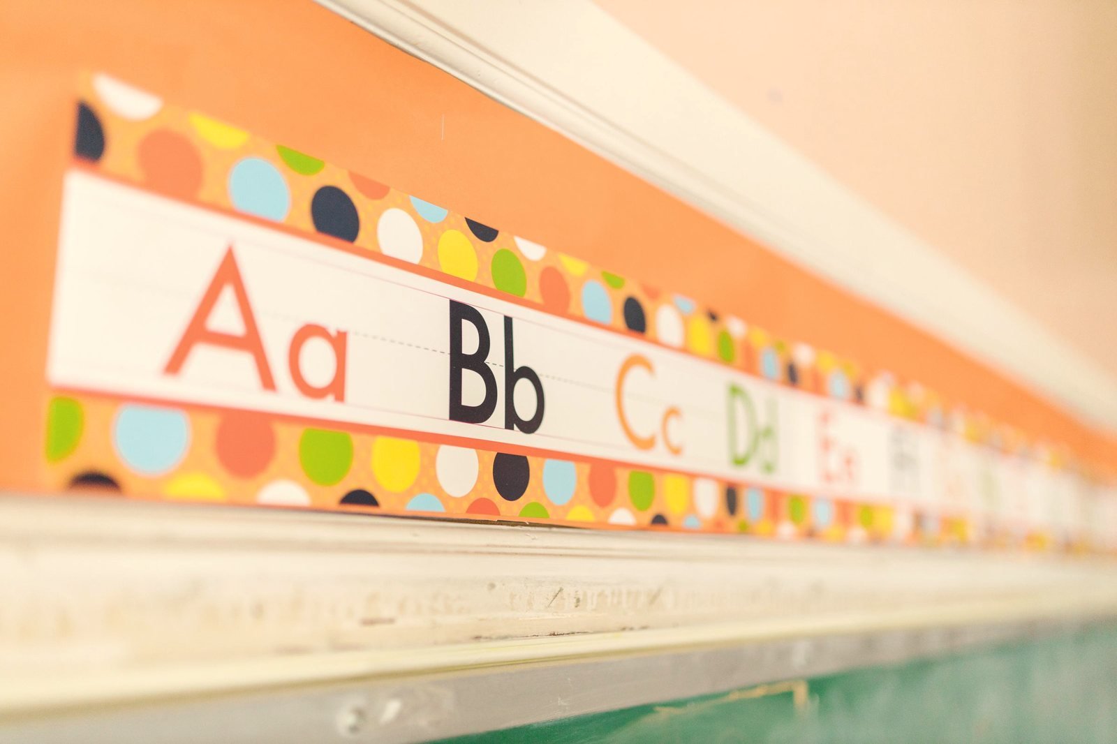 A printed alphabet strip running along a classroom wall above a chalkboard.
