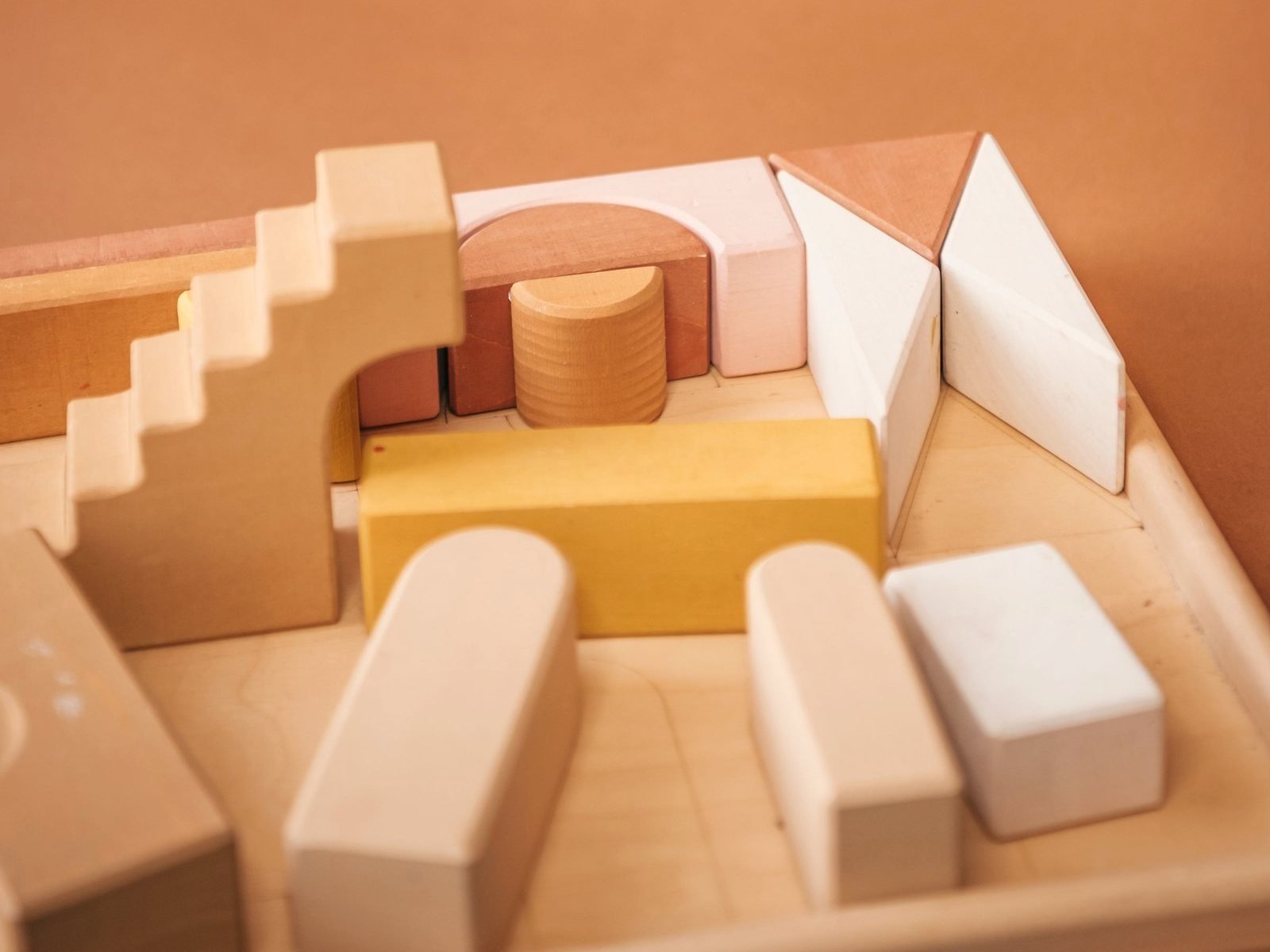 Wooden building blocks arranged in a tray against a warm wall.