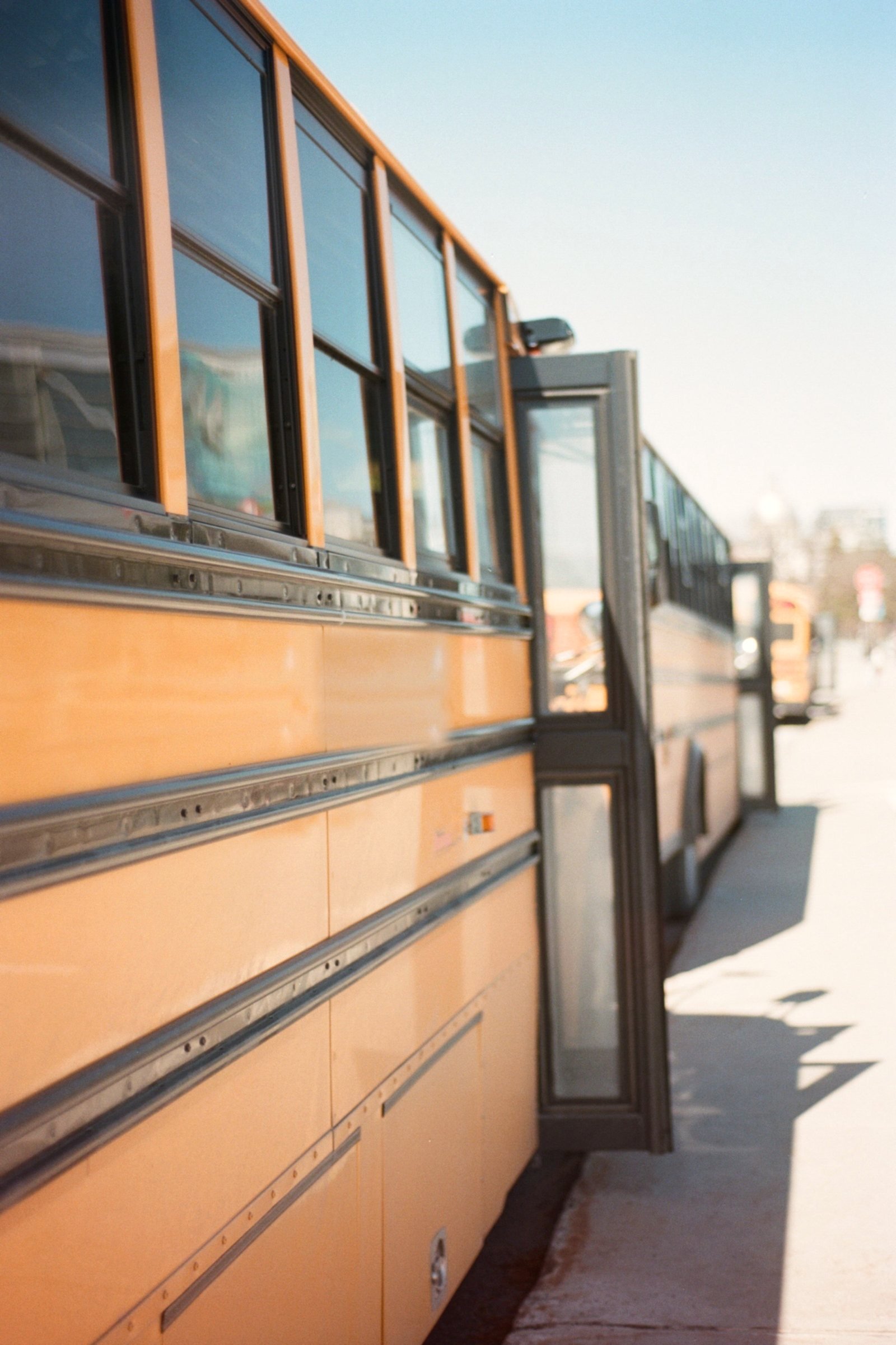 The side of a yellow school bus parked at the kerb with its door open.
