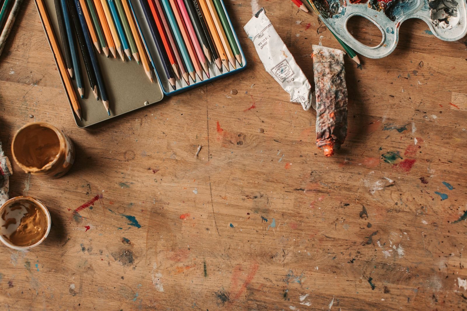 Coloured pencils, paint tubes and jars on a well used wooden craft table.